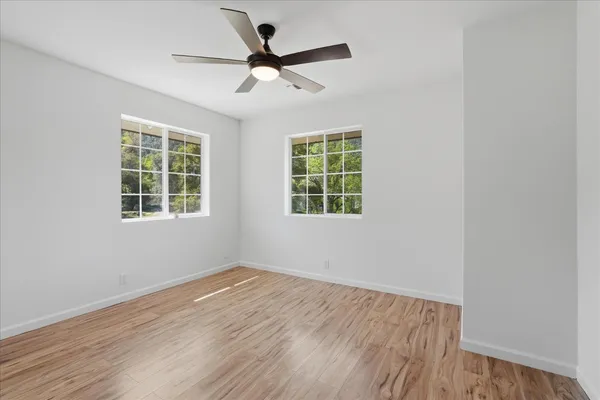 an empty room with wooden floor ceiling fan and windows