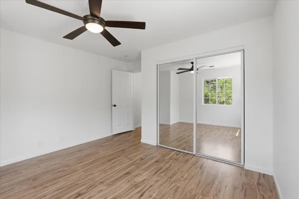 an empty room with wooden floor fan and windows