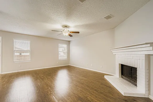 a view of an empty room with wooden floor fireplace and a window