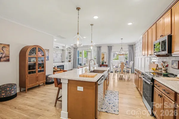 a room with stainless steel appliances kitchen island granite countertop a stove top oven a sink a dining table and chairs with wooden floor