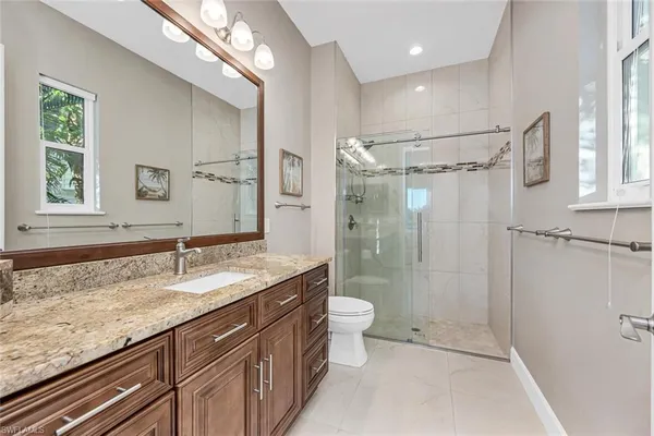 a bathroom with a granite countertop sink a mirror a toilet and shower