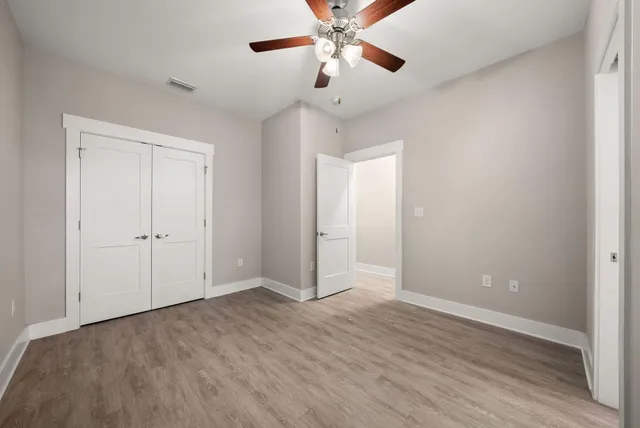 an empty room with wooden floor chandelier fan and windows