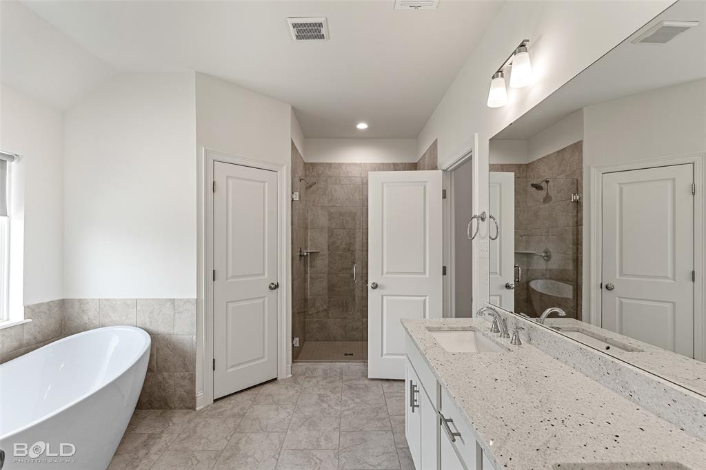 304 Prien Lk Loop Bossier City, LA 71111 - Photo 25 of 39 Contemporary bathroom featuring a white freestanding soaking tub, a tiled walk-in shower with glass enclosure, and a dual-sink vanity with a speckled countertop and integrated mirror