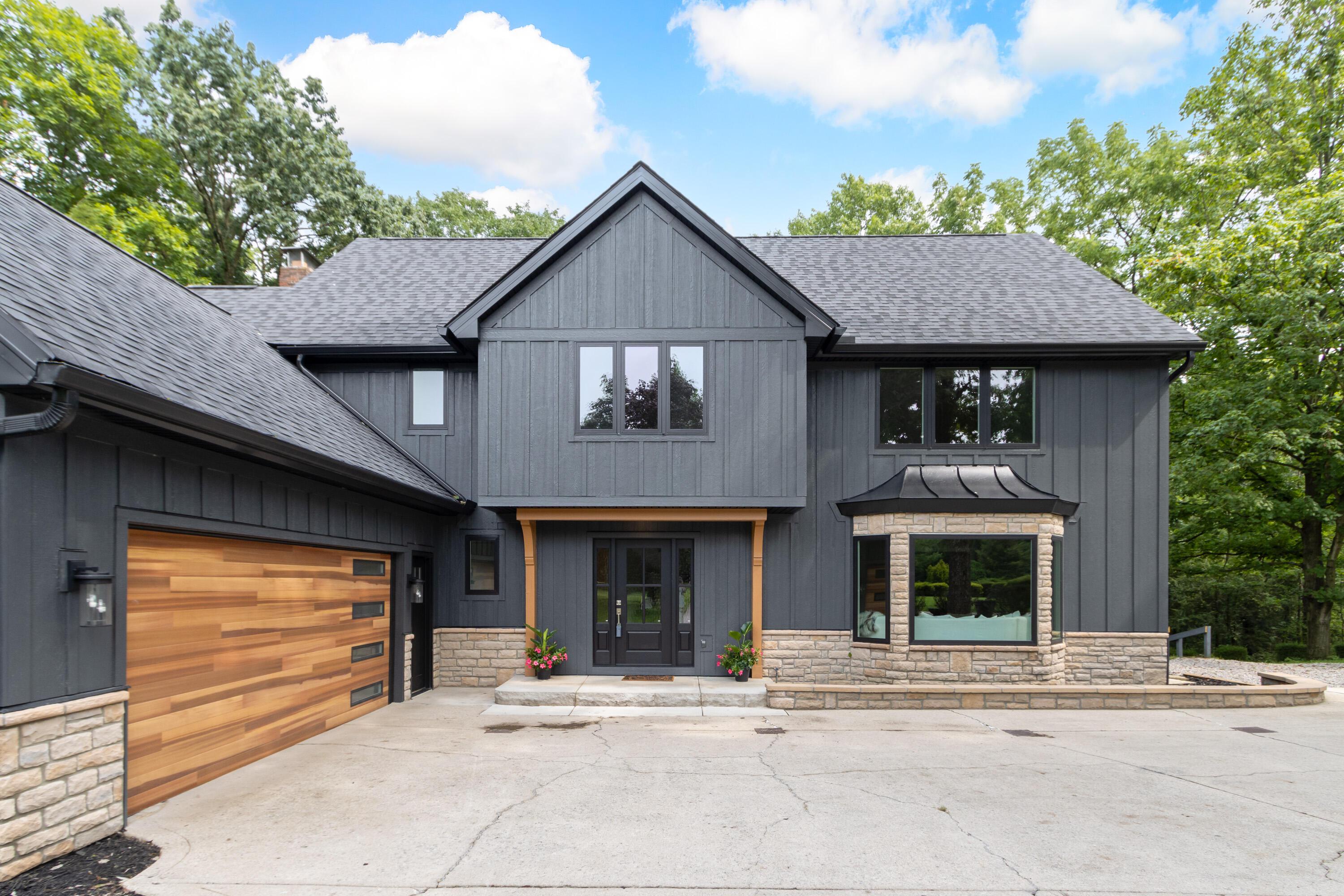 1560 Carriage Road Powell, OH 43065 - Photo 6 of 73 Modern exterior featuring dark vertical siding, a wood-finish garage door, stone accents, a bay window with a curved metal roof, and a covered entry