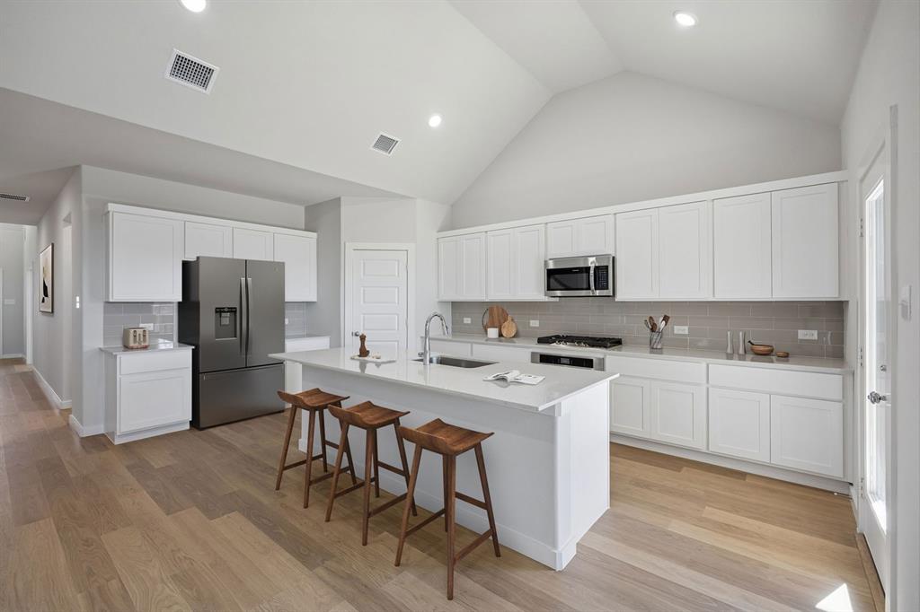 1461 Companero Street Haslet, TX 76052 - Photo 7 of 35 a kitchen with stainless steel appliances a stove a sink dishwasher a refrigerator and white cabinets with wooden floor
