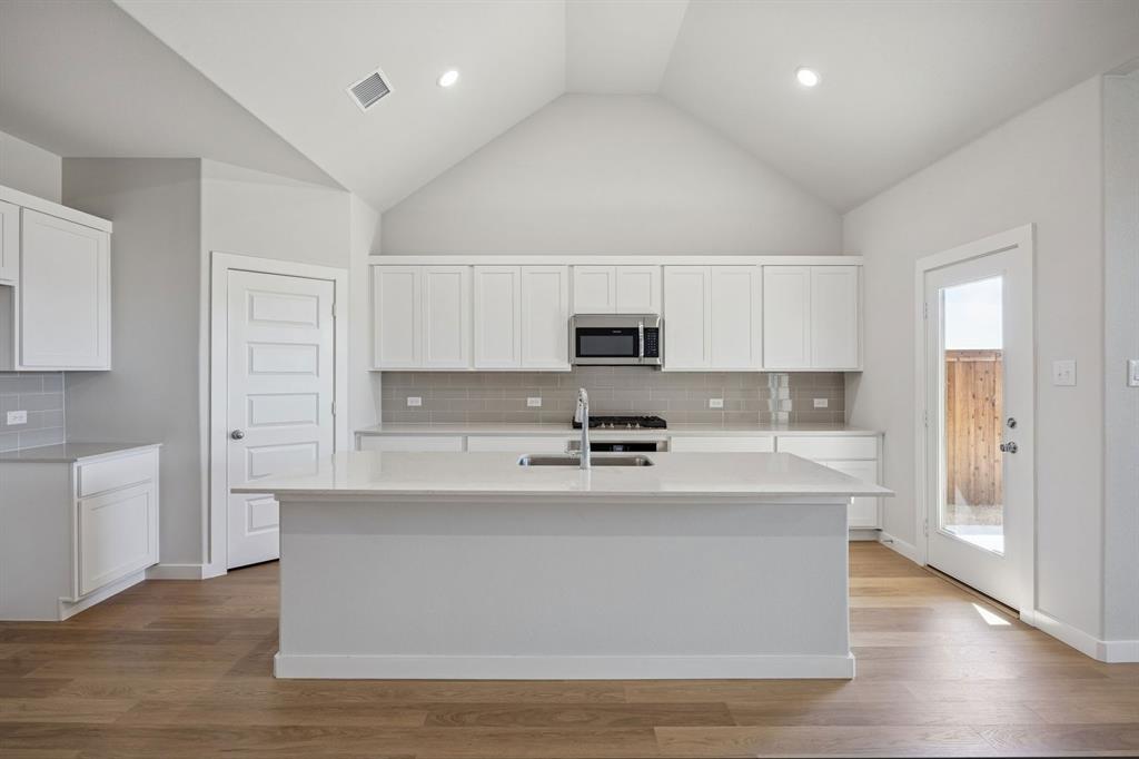 1461 Companero Street Haslet, TX 76052 - Photo 8 of 35 a large kitchen with stainless steel appliances granite countertop a stove a sink a refrigerator and white cabinets with wooden floor