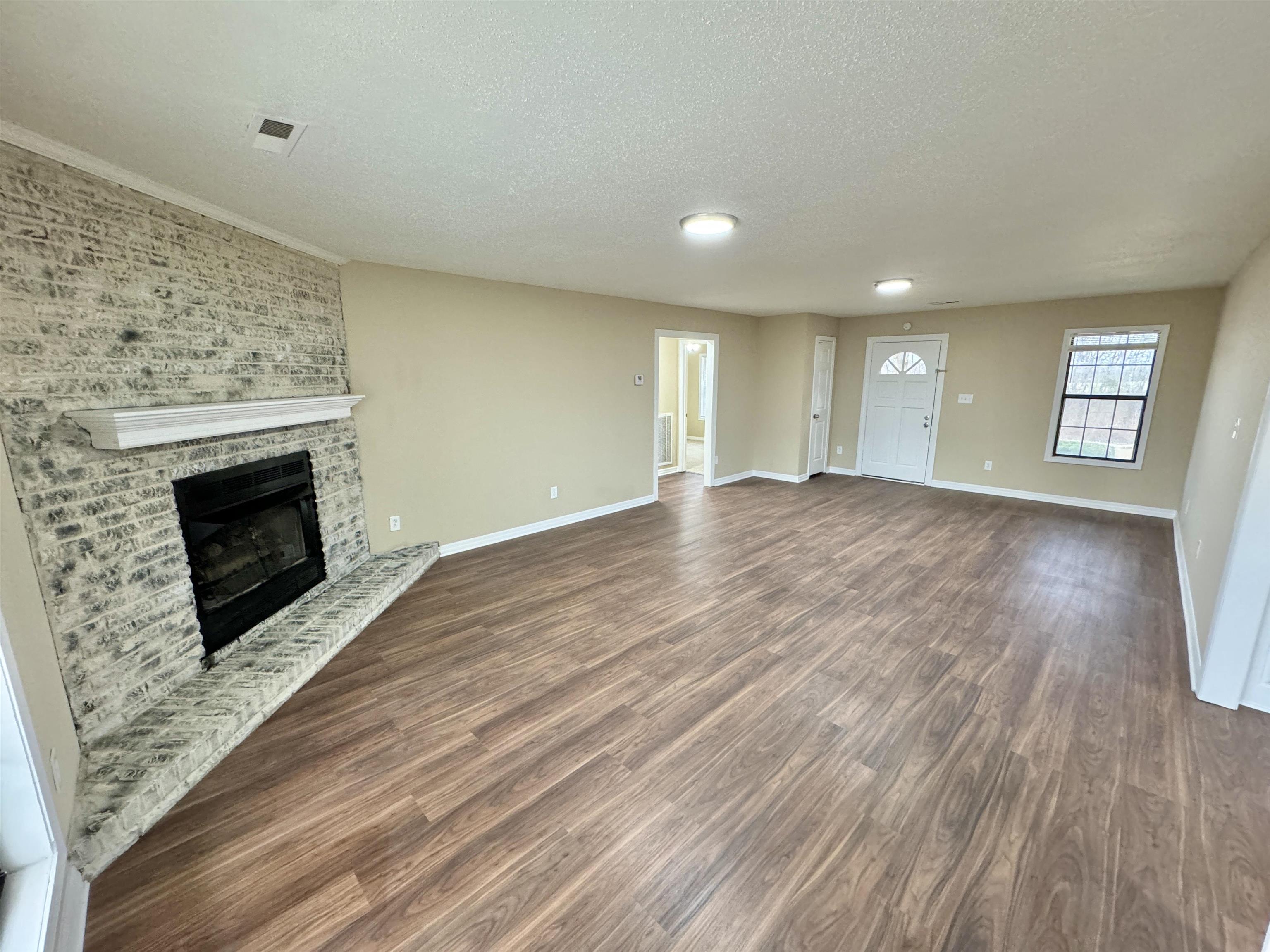 6889 Fulton Road Brownsville, TN 38012 - Photo 11 of 40 Unfurnished living room with a brick fireplace, dark wood-type flooring, and a textured ceiling
