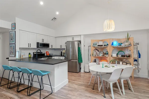 a kitchen with stainless steel appliances a dining table chairs stove refrigerator and cabinets