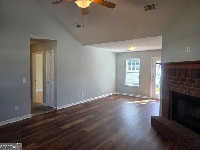 a view of an empty room with wooden floor fireplace and a window