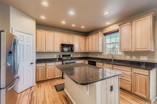 a kitchen with kitchen island granite countertop stainless steel appliances a sink stove refrigerator and cabinets
