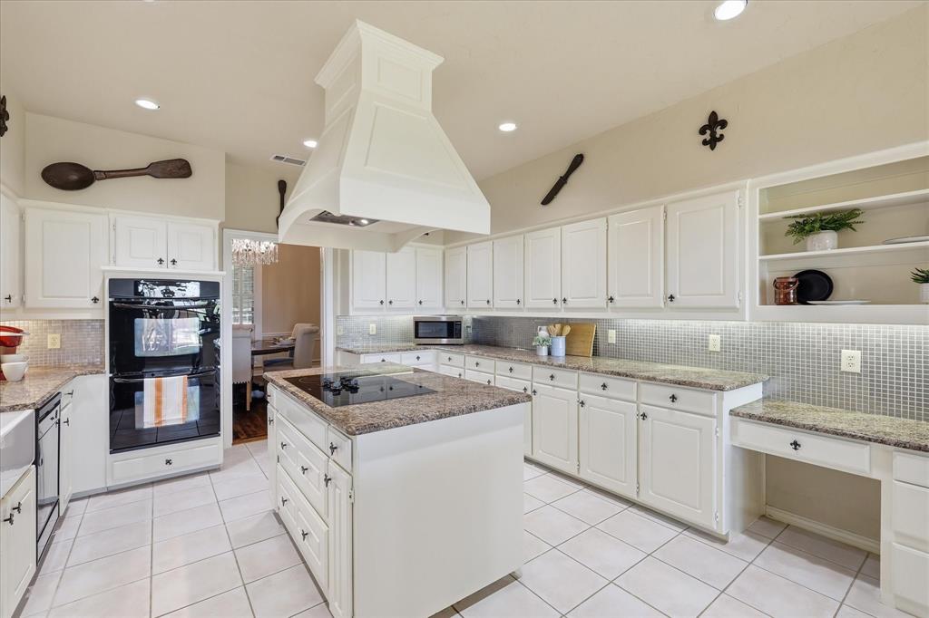 6955 Hawk Road Flower Mound, TX 75022 - Photo 18 of 40 Spacious kitchen featuring an expansive island with an integrated cooktop, white cabinetry, double wall ovens, granite countertops, and a full tile backsplash