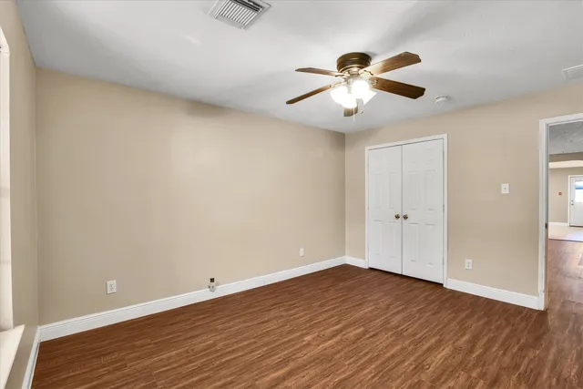 a view of an empty room with wooden floor and a ceiling fan