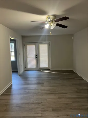 a view of an empty room with wooden floor and fan