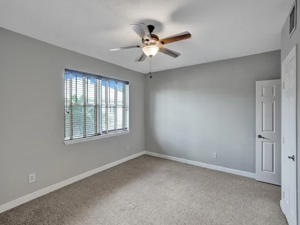 an empty room with chandelier fan and windows