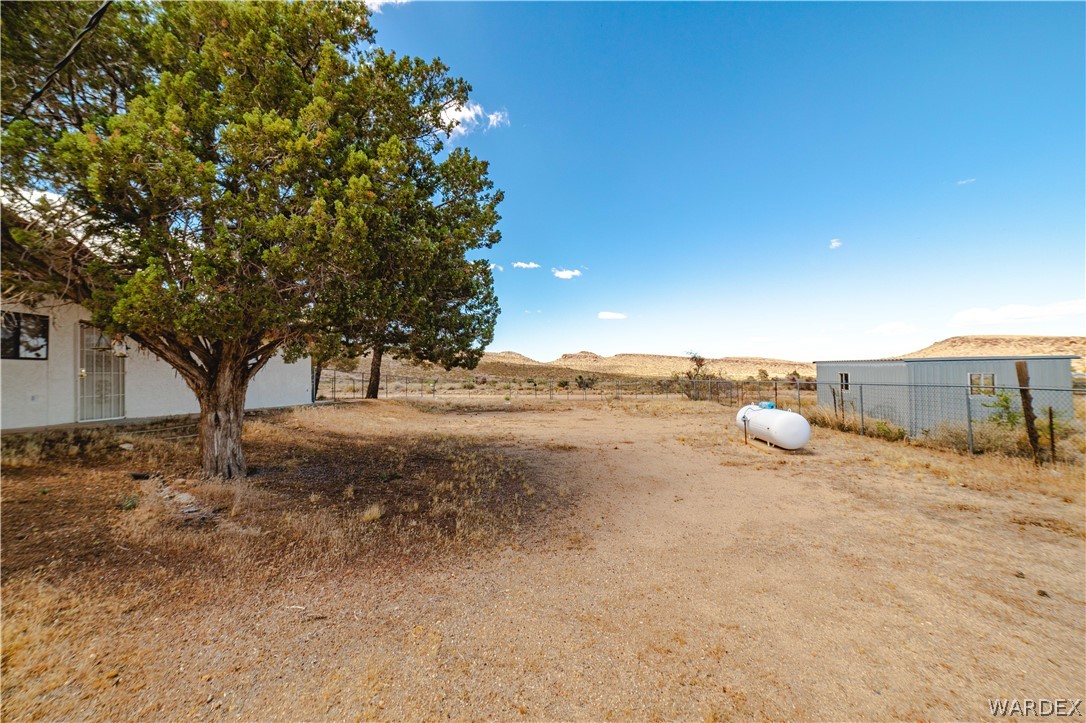 2100 East Valley View Road Kingman, AZ 86409 - Photo 49 of 53 Expansive dryland property featuring a mature juniper tree, a white-sided structure with security doors, a metal outbuilding with a window, a chain-link fence, and a large propane tank