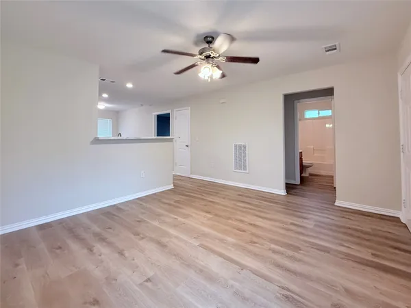 a view of an empty room with wooden floor and a ceiling fan