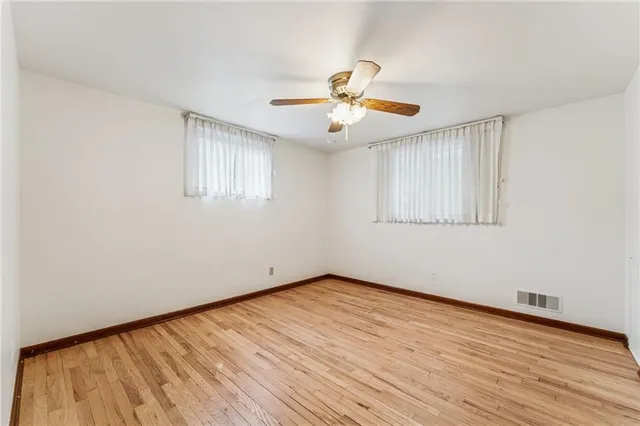 an empty room with wooden floor chandelier fan and windows