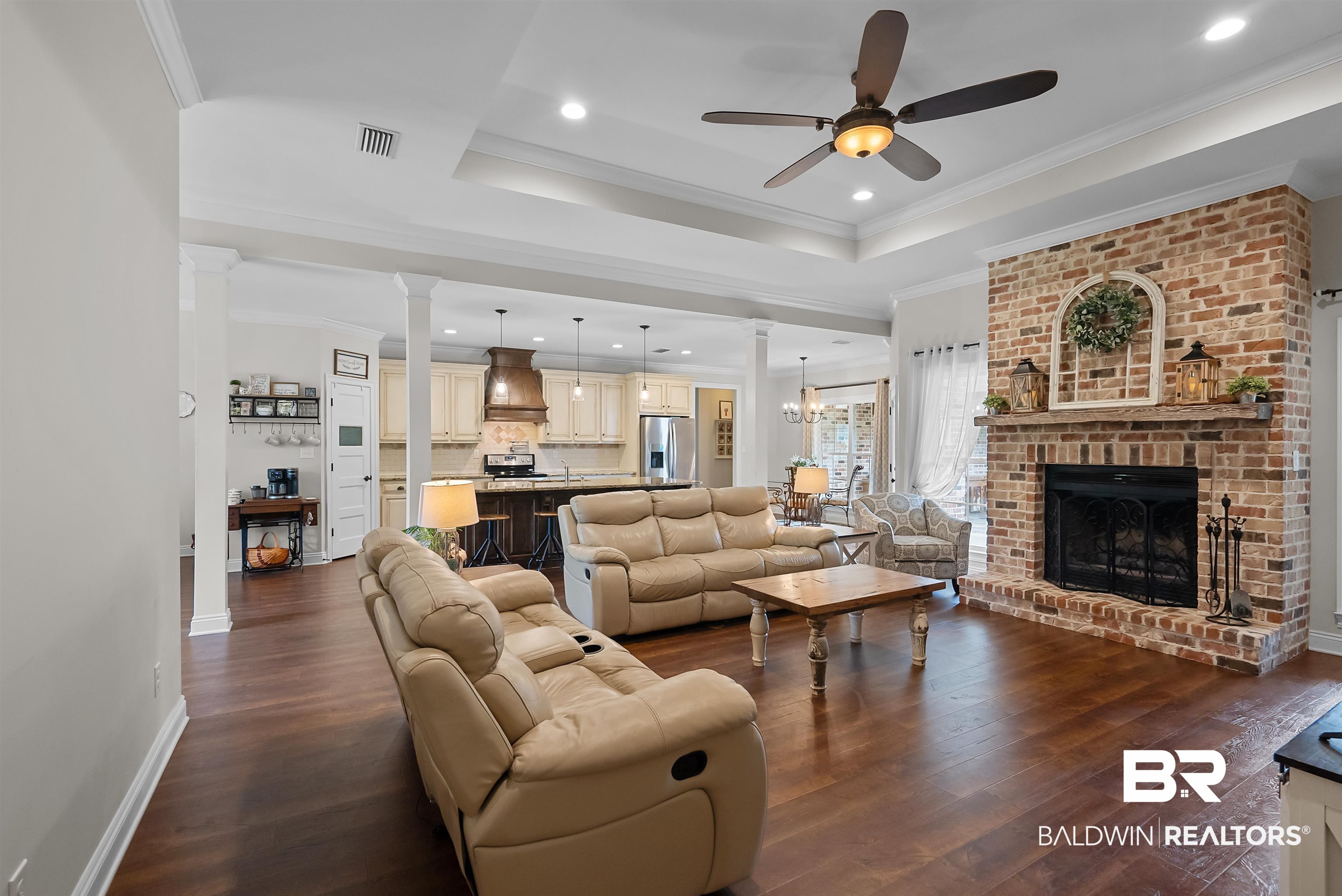 12070 Comalander Road Fairhope, AL 36532 - Photo 11 of 50 Spacious living area featuring wood-finish flooring, a brick fireplace with a mantel, and a tray ceiling with a ceiling fan