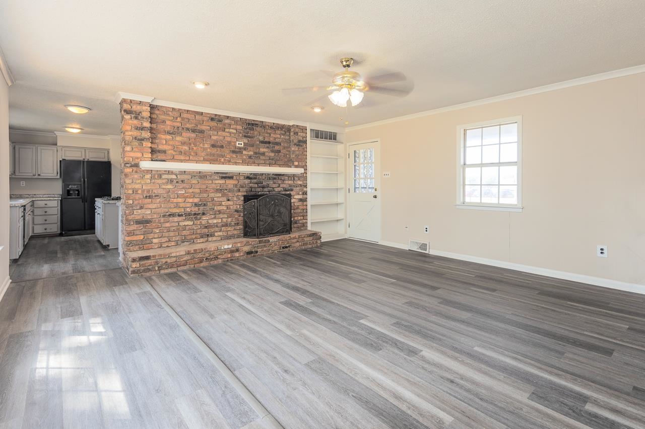 2718 Kate Bond Road Memphis, TN 38133 - Photo 3 of 39 Unfurnished living room featuring crown molding, a brick fireplace, dark wood-style floors, a ceiling fan, and built in shelves