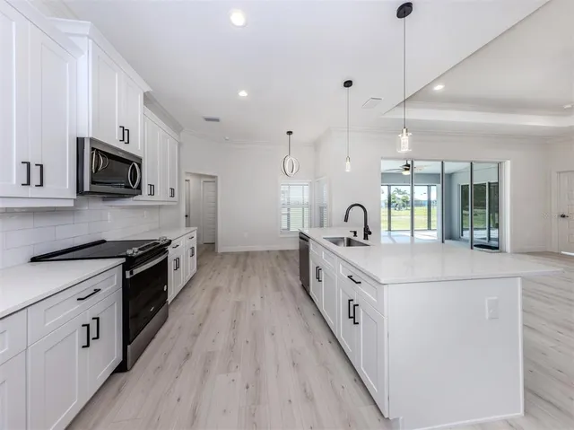 a large white kitchen with stainless steel appliances granite countertop lots of white cabinets a sink and a wooden floor