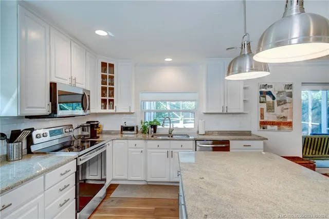 a kitchen with kitchen island granite countertop a sink cabinets stainless steel appliances and a window