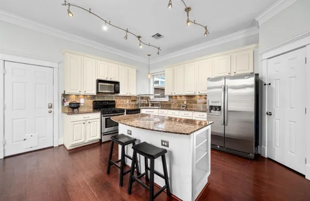 a kitchen with granite countertop a refrigerator a stove a microwave oven a sink dishwasher and white cabinets with wooden floor