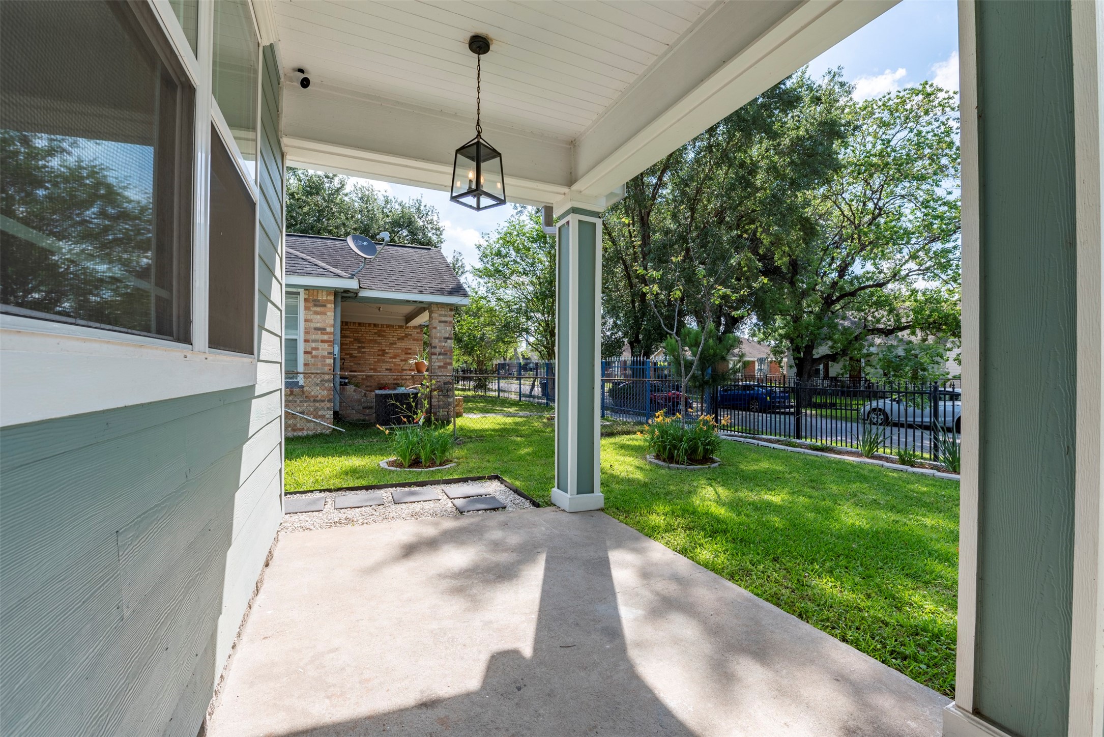 109 Dresden Street Houston, TX 77012 - Photo 42 of 43 This photo showcases a charming covered porch with a hanging light, opening to a lush green backyard. The space is bordered by a fence and surrounded by mature trees, offering a peaceful outdoor retreat.