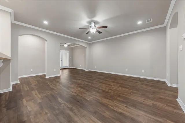 a view of an empty room with wooden floor and a ceiling fan