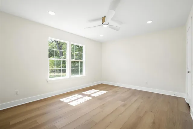 an empty room with wooden floor chandelier fan and windows