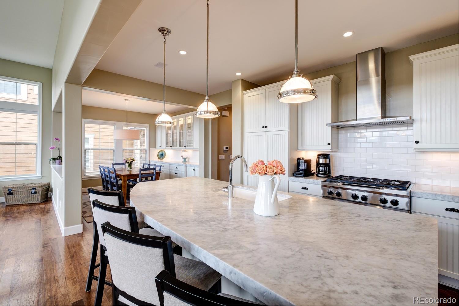 10711 Sundial Rim Road Highlands Ranch, CO 80126 - Photo 5 of 35 a kitchen with stainless steel appliances granite countertop a stove a kitchen island a dining table and chairs with wooden floor