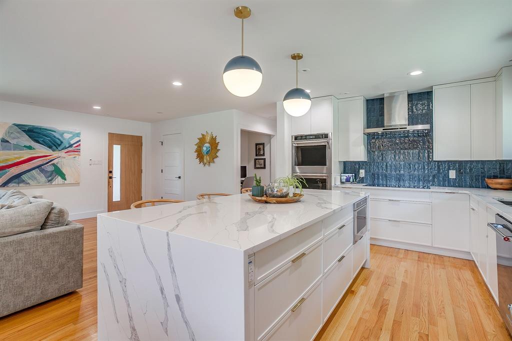 6700 Fortune Road Fort Worth, TX 76116 - Photo 9 of 40 Kitchen featuring an oversized waterfall island with an integrated microwave, white cabinetry, a blue textured tile backsplash, stainless steel appliances, and wood-finish flooring