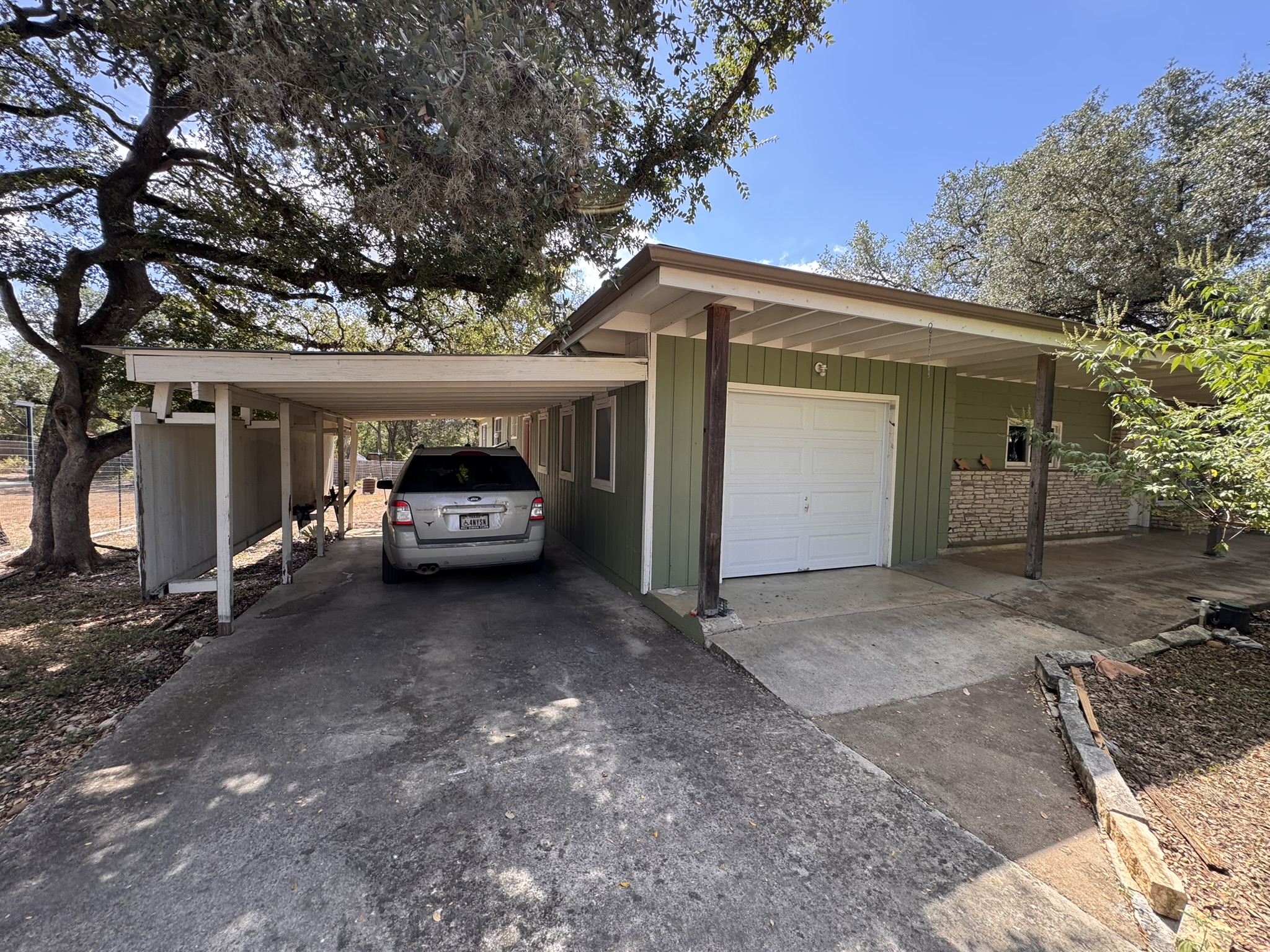 13 Presidio Road Wimberley, TX 78676 - Photo 7 of 7 Mature trees shade a functional driveway featuring an attached garage and a covered carport.