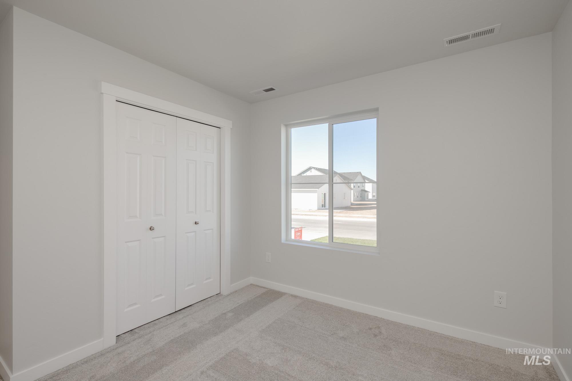 14092 Shiny Spruce Street Caldwell, ID 83607 - Photo 15 of 22 Neutral-toned room featuring a large window with white trim, light gray carpeting, and a white bi-fold closet