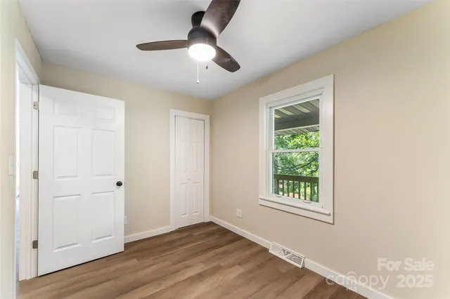 an empty room with wooden floor chandelier fan and windows