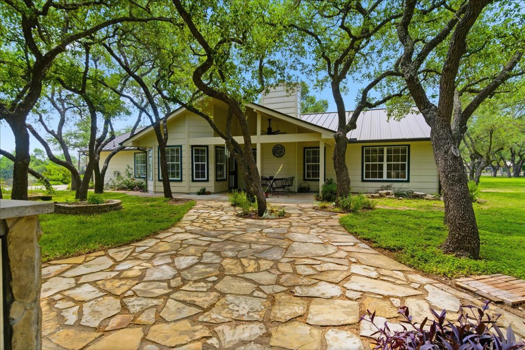 Inviting stone walkway leading to the rear cover patio, surrounded by established trees and curated landscape beds.