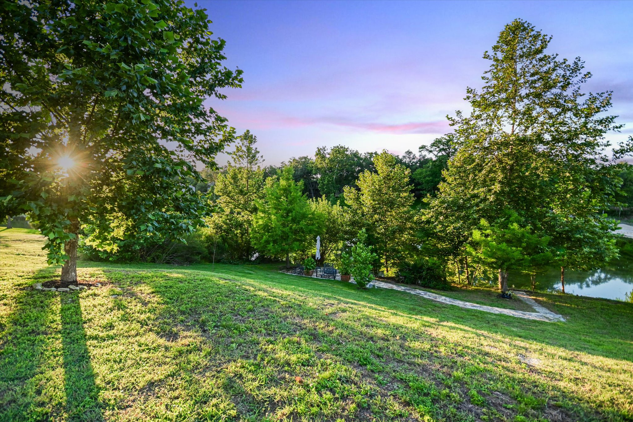 2411 Spoke Hollow Road Wimberley, TX 78676 - Photo 26 of 37 Discover a tranquil backyard oasis featuring a lush lawn, mature trees, and a serene water view.