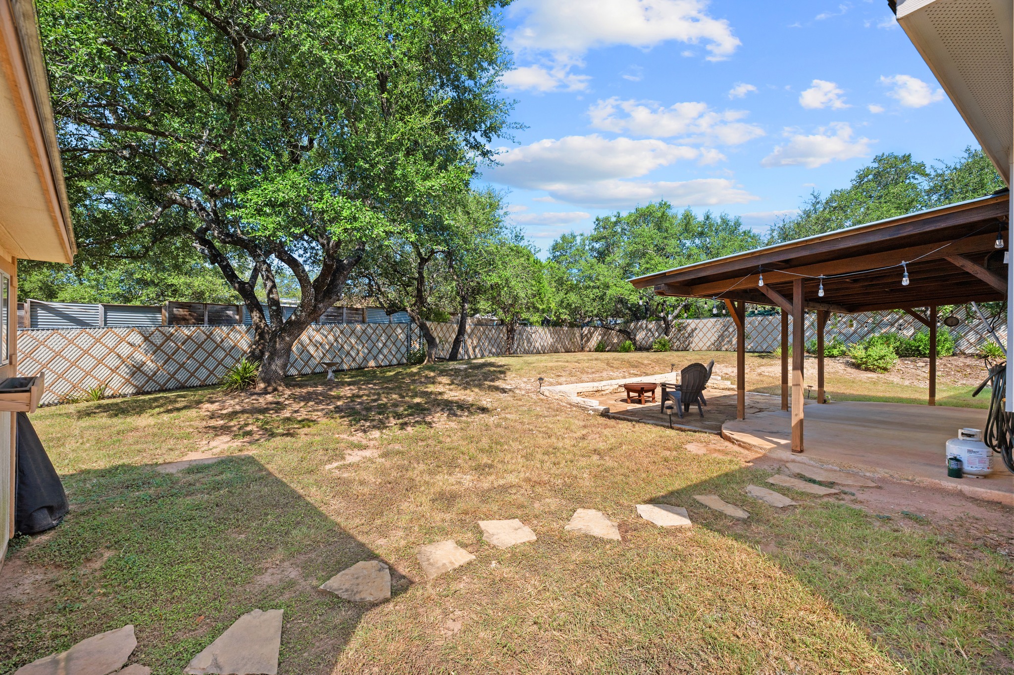 10114 Janet Loop Dripping Springs, TX 78620 - Photo 26 of 34 Mature trees shade a spacious lawn featuring a covered patio and stone pathways.