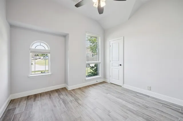 an empty room with wooden floor chandelier fan and windows