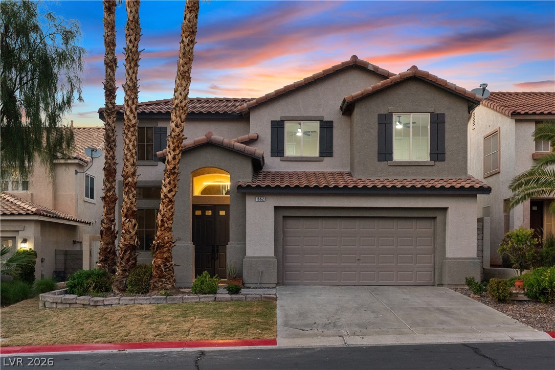 1662 Ravanusa Drive Henderson, NV 89052 - Photo 2 of 74 A striking stucco facade with tile roof accents and welcoming entry under a vibrant sunset.