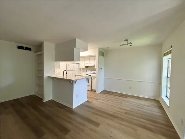 a room with kitchen island granite countertop wooden floors and white cabinets