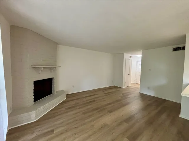a view of an empty room with wooden floor fireplace and a window