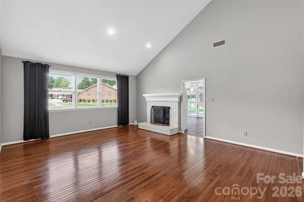an empty room with wooden floor fireplace and windows