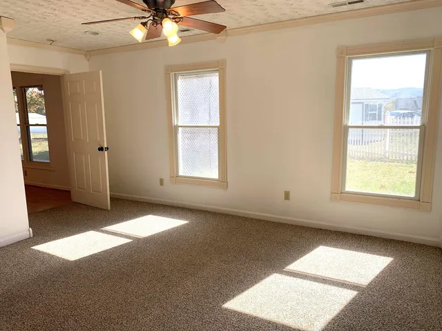 an empty room with chandelier fan and windows