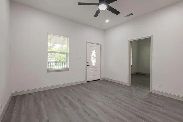an empty room with wooden floor chandelier fan and windows
