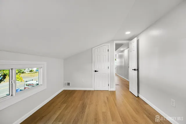 a view of a refrigerator in kitchen and an empty room with wooden floor