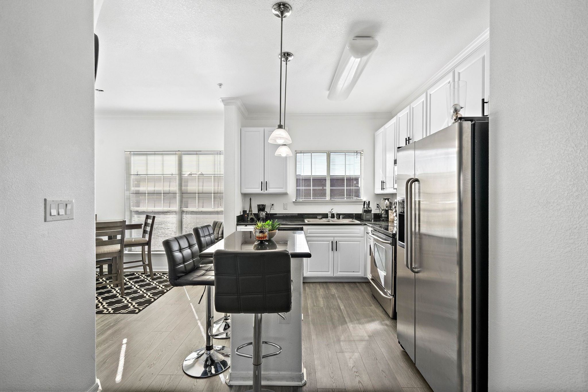 9200 Westheimer Road, Unit 203 Houston, TX 77063 - Photo 2 of 10 This photo showcases a modern kitchen with white cabinets, stainless steel appliances, and a breakfast bar. The space is bright and open, with natural light from large windows. The kitchen flows into the open concept living area.