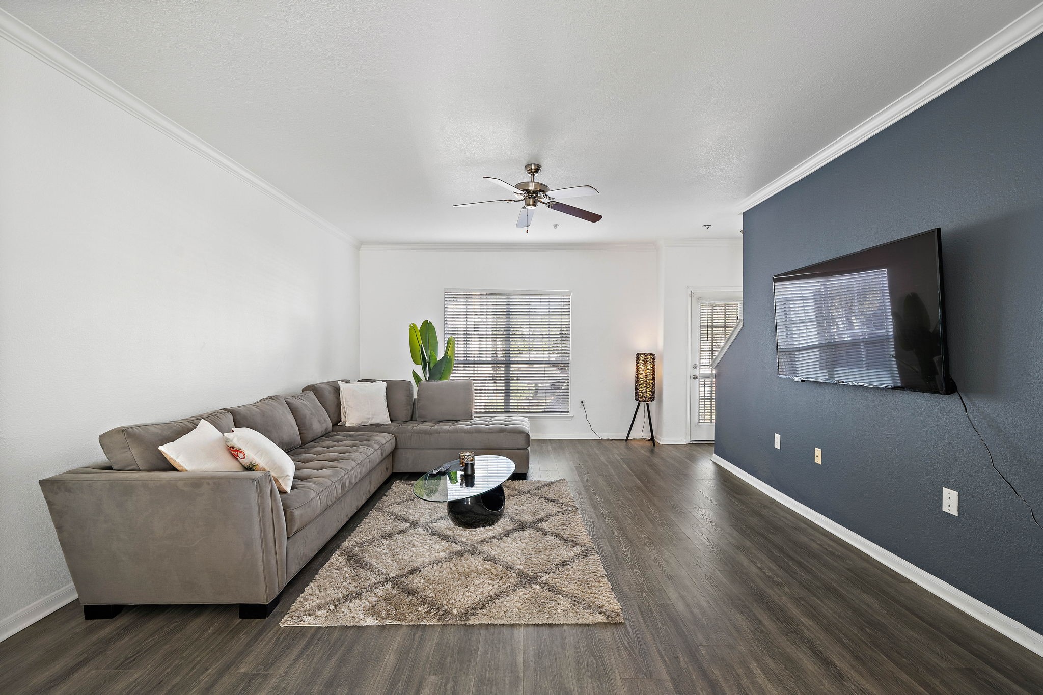 9200 Westheimer Road, Unit 203 Houston, TX 77063 - Photo 4 of 10 Spacious living room with dark wood flooring and spacious enough to accomendate a large sectional sofa or multiple sitting areas. It has a ceiling fan, and natural light from a window and glass door, offering a cozy yet contemporary feel.
