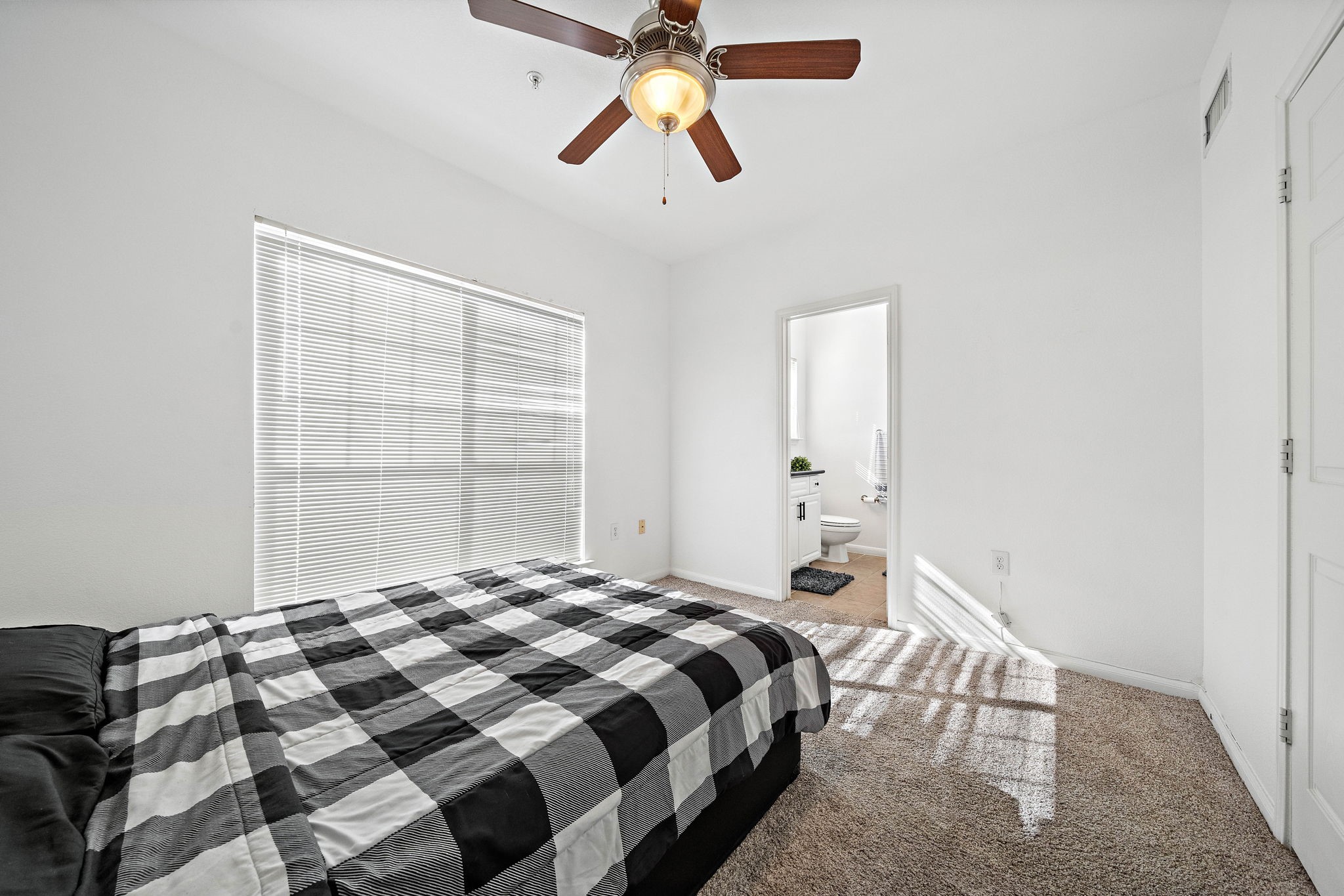 9200 Westheimer Road, Unit 203 Houston, TX 77063 - Photo 8 of 10 This is a bright bedroom featuring a large window with blinds, carpeted flooring, and a ceiling fan. It includes an en-suite bathroom, providing convenience and privacy. The overall ambiance is clean and inviting.