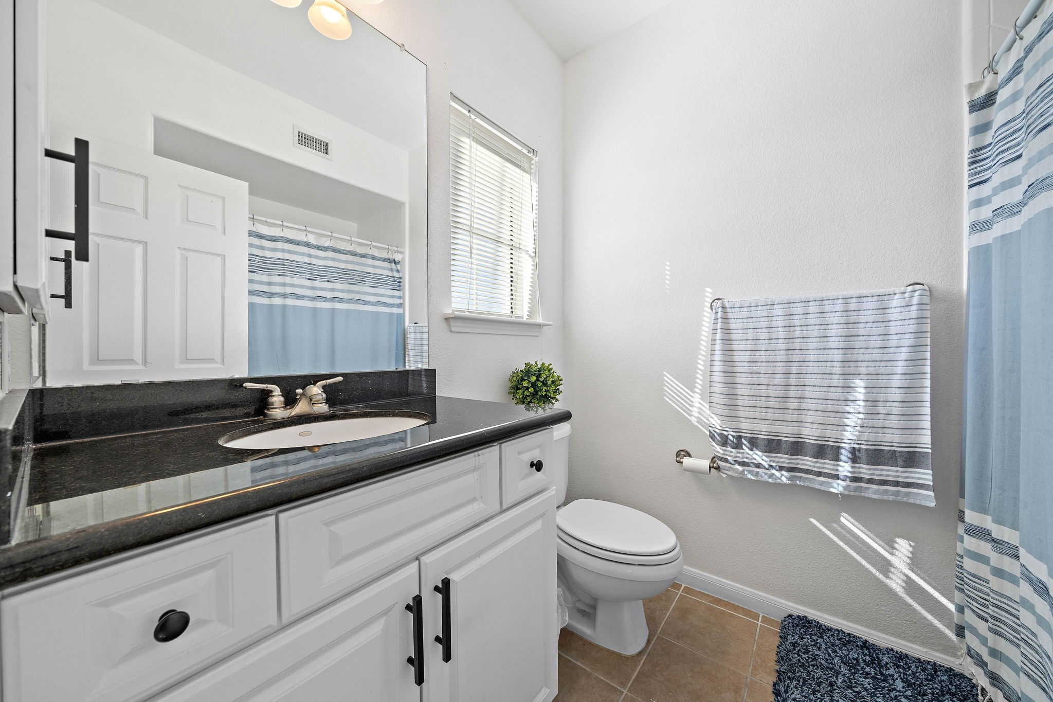 9200 Westheimer Road, Unit 203 Houston, TX 77063 - Photo 9 of 10 This bathroom features a modern design with a sleek black countertop, white cabinetry, and a large mirror. It includes a bath/shower, tile flooring, and a window for natural light. Perfect for a refreshing and functional space.