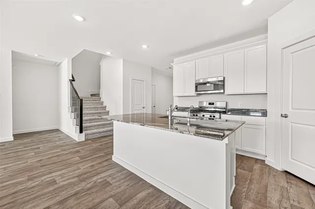 a kitchen with stainless steel appliances a stove top oven a sink a refrigerator and white cabinets with wooden floor